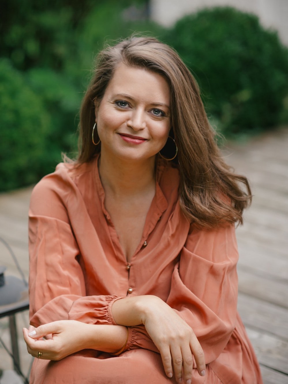 Marion sitzt im Garten und schaut lächelnd in die Kamera
